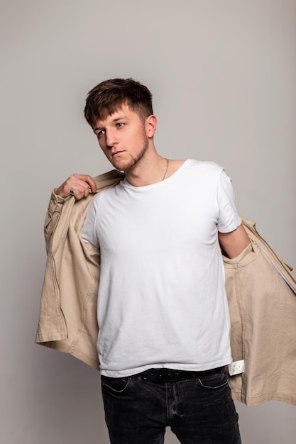 Beau jeune homme élégant avec une coiffure dans des vêtements décontractés à la mode avec un t-shirt blanc habille une veste de mode dans le studio