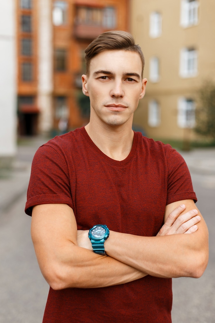 Photo beau jeune homme élégant dans un t-shirt à la mode rouge avec une coiffure élégante se promène dans la ville par une chaude journée d'été