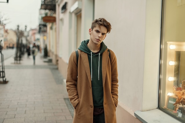 Beau jeune homme élégant avec un manteau d'automne vintage près de la devanture avec ampoules