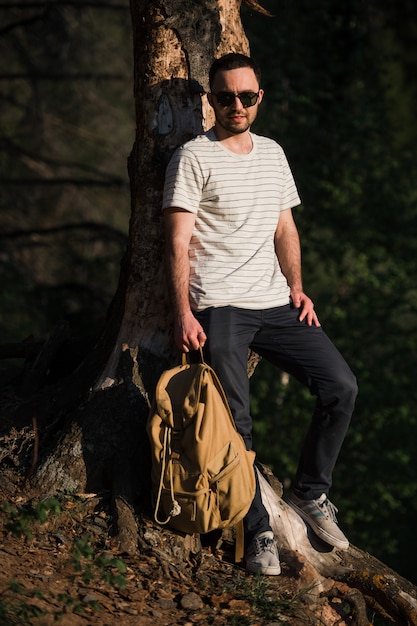 Beau jeune homme élégant portant avec sac à dos à la main voyage dans la forêt