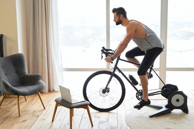 Photo beau jeune homme faisant du vélo d'exercice stationnaire