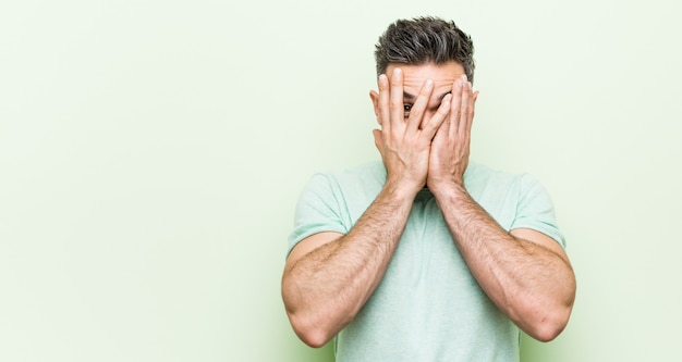 Beau jeune homme sur un fond vert cligner des yeux effrayé et nerveux.