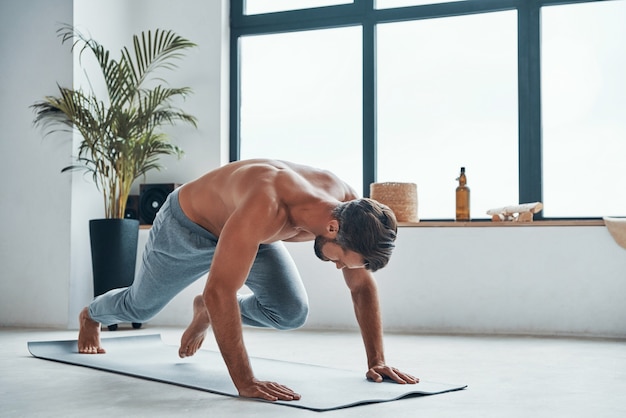 Beau jeune homme gardant la position de la planche tout en faisant de l'exercice à la maison