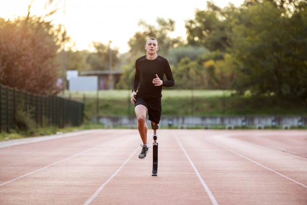 Beau jeune homme handicapé caucasien sportif en tenue de sport et avec une jambe artificielle en cours d'exécution sur une piste de course sur le stade.