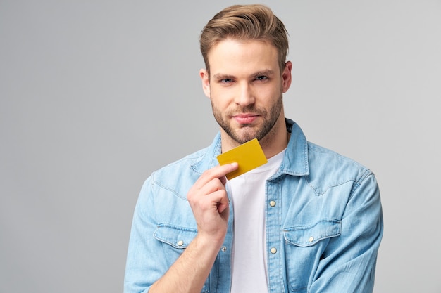 Beau jeune homme heureux montrant une carte de réduction vierge de banque cor