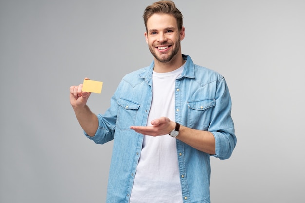 Beau jeune homme heureux montrant une carte de réduction vierge de banque cor