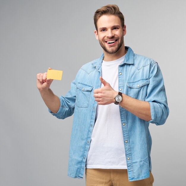 Beau jeune homme heureux montrant une carte de réduction vierge de banque cor