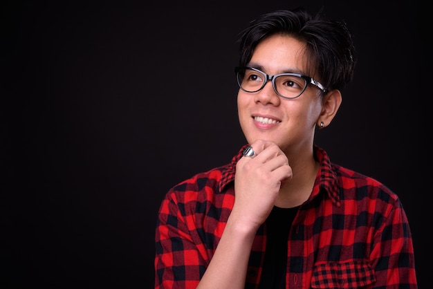 Beau jeune homme hipster philippin avec des lunettes contre le mur noir