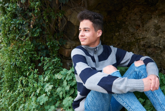 Un beau jeune homme hispanique portant un pull et un jean déchiré assis à l'extérieur