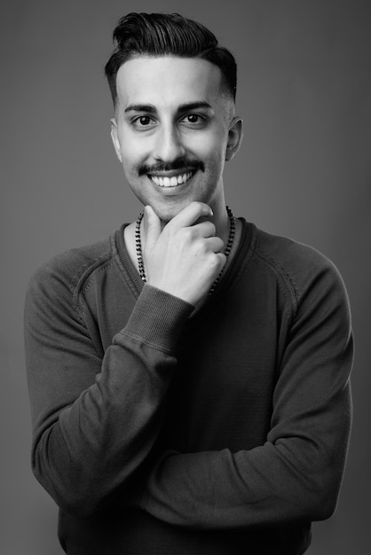 Beau jeune homme iranien avec moustache avec chemise à manches longues contre mur gris en noir et blanc