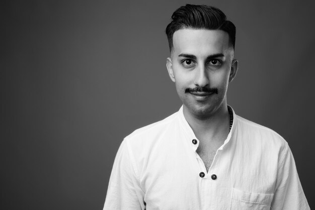Beau jeune homme iranien avec moustache portant une chemise blanche contre un mur gris en noir et blanc