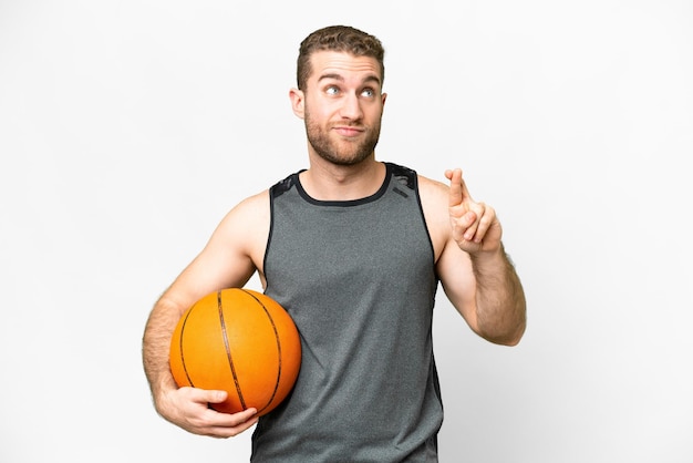 Beau jeune homme jouant au basket-ball sur fond blanc isolé avec les doigts croisés et souhaitant le meilleur