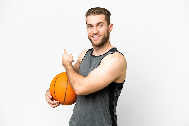 Beau jeune homme jouant au basket-ball sur fond blanc isolé pointant vers l'arrière