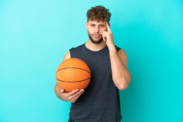 Beau jeune homme jouant au basket isolé sur fond bleu en pensant à une idée