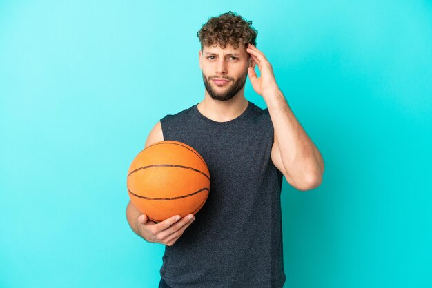 Beau jeune homme jouant au basketball isolé sur fond bleu ayant des doutes