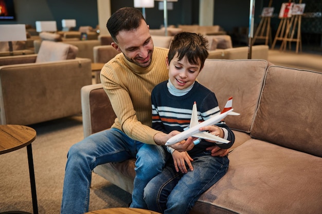 Beau jeune homme jouant à l'avion de jouets avec son jeune frère tout en se reposant dans le salon VIP du terminal de départ de l'aéroport pendant un voyage en famille