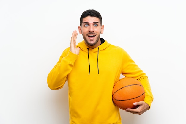 Beau jeune homme de joueur de basket sur un mur blanc isolé avec une expression faciale surprise et choquée