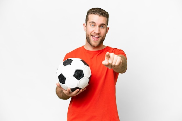 Beau jeune homme de joueur de football sur fond blanc isolé surpris et pointant vers l'avant