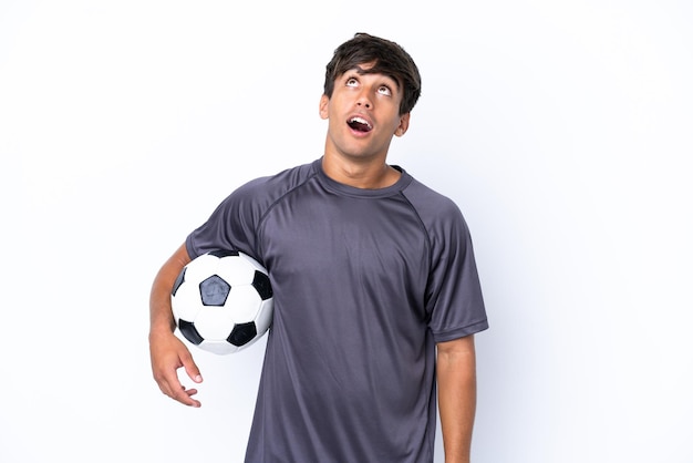 Beau jeune homme de joueur de football isolé sur fond blanc en levant et avec une expression surprise