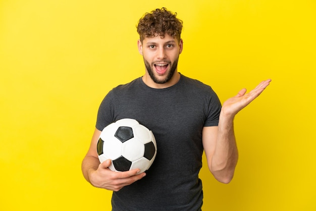 Beau jeune homme de joueur de football isolé sur fond jaune avec une expression faciale choquée