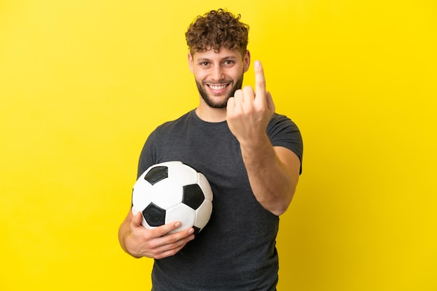 Beau jeune homme de joueur de football isolé sur fond jaune faisant un geste à venir