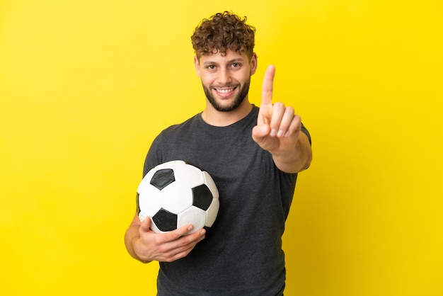 Beau jeune homme de joueur de football isolé sur fond jaune montrant et levant un doigt