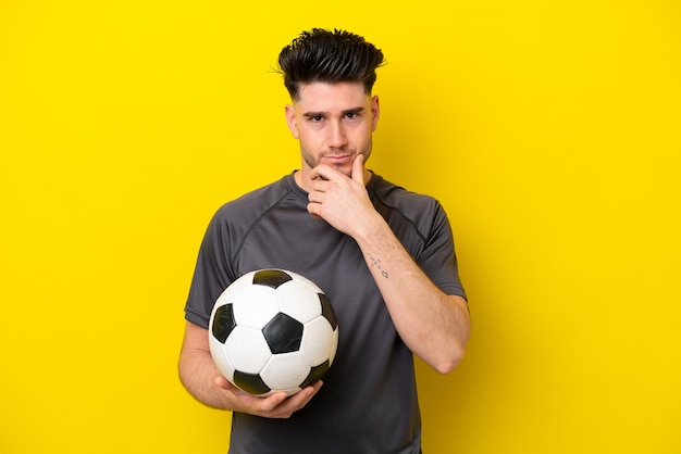 Beau jeune homme de joueur de football isolé sur fond jaune pensant