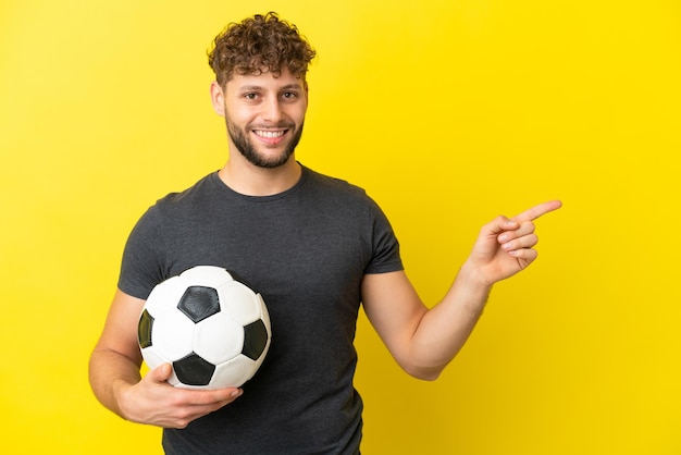 Beau jeune homme de joueur de football isolé sur fond jaune pointant le doigt sur le côté