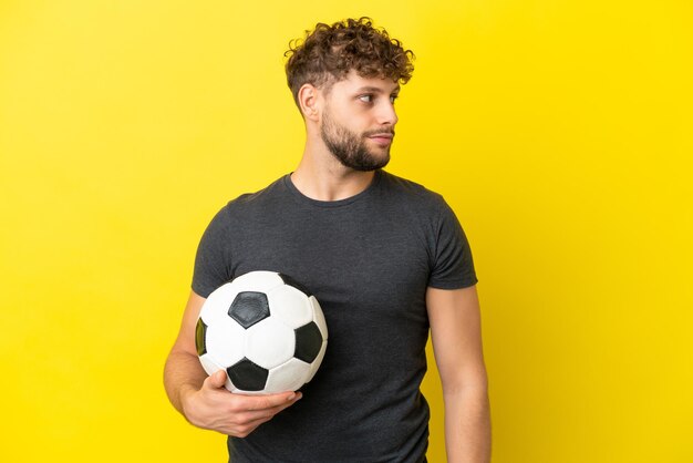 Beau jeune homme de joueur de football isolé sur fond jaune regardant sur le côté