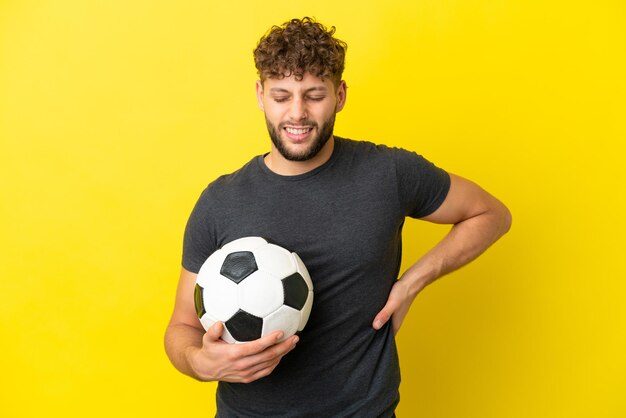 Beau jeune homme de joueur de football isolé sur fond jaune souffrant de maux de dos pour avoir fait un effort