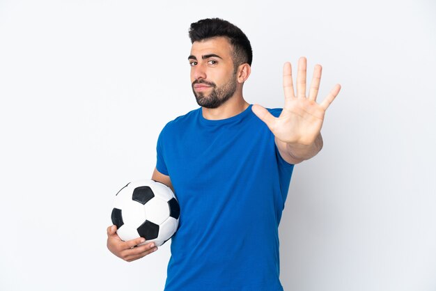 Beau jeune homme joueur de football sur mur isolé comptant cinq avec les doigts