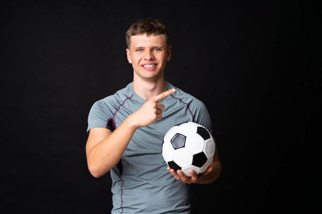 Beau jeune homme joueur de football sur mur noir isolé