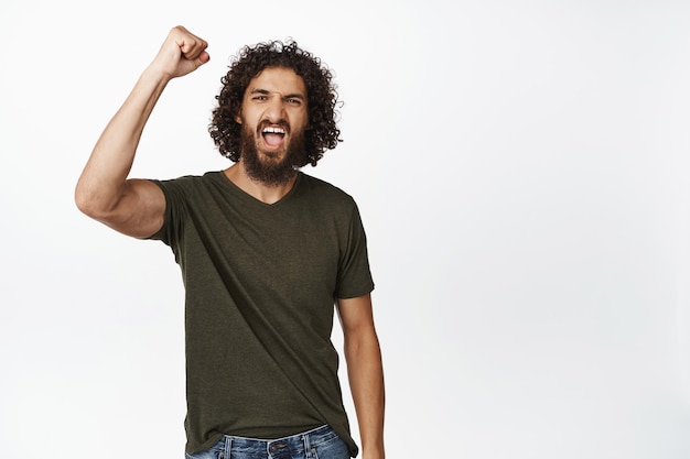 Beau jeune homme levant le poing fermé et criant pour protester Activiste masculin chantant debout sur fond blanc