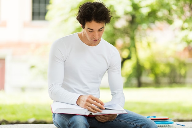 Beau jeune homme lisant un livre sur un banc dans le parc