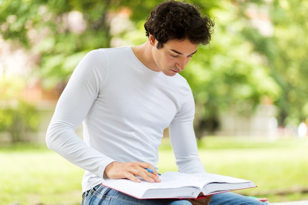 Beau jeune homme lisant un livre sur un banc dans le parc