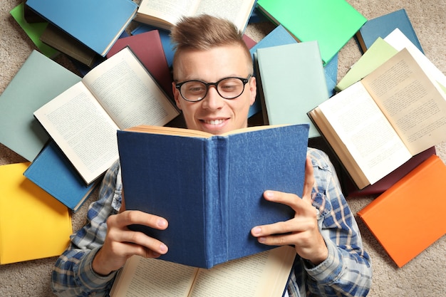 Beau jeune homme lisant un livre en position couchée sur le sol