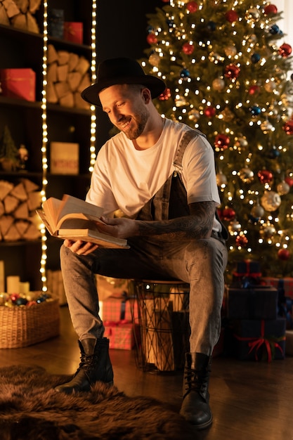 beau jeune homme lisant un livre près de sapin de Noël à la maison.