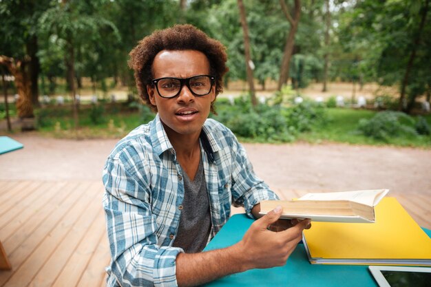 Beau jeune homme à lunettes lire et apprendre dans un café en plein air