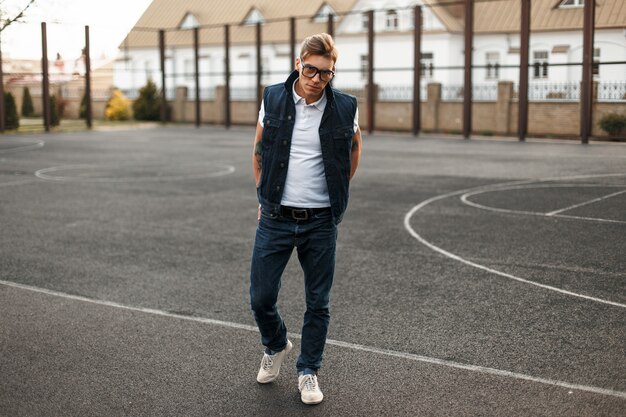 Beau jeune homme avec des lunettes de style jeans vintage marchant le long de la rue