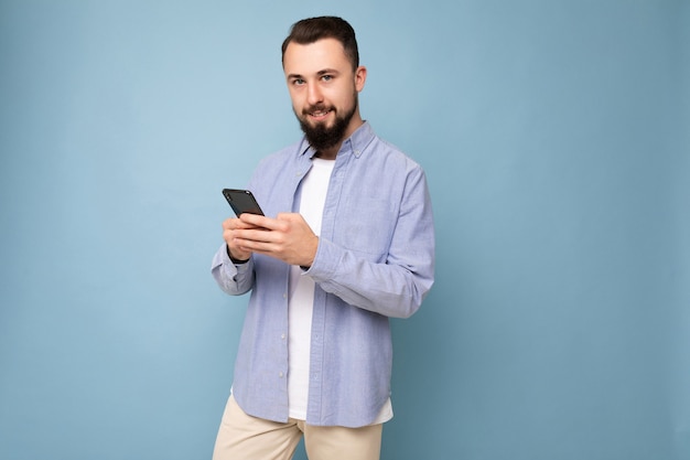 Beau jeune homme mal rasé brune avec barbe portant un t-shirt blanc élégant et une chemise bleue isolée