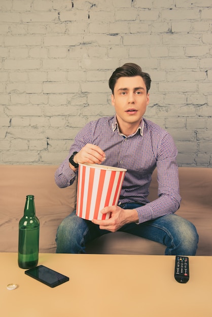 Beau jeune homme mangeant du pop-corn et regarder la télévision