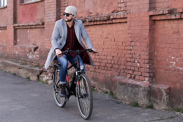 Beau jeune homme en manteau gris et chapeau montant une rue cyclable dans la ville.