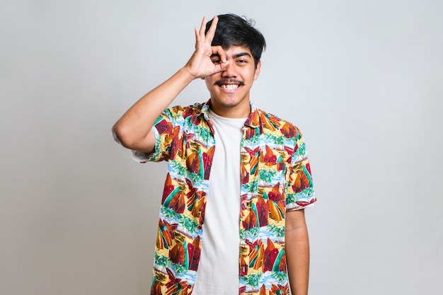 Beau jeune homme avec moustache portant un tshirt décontracté sur fond blanc souriant positif faisant signe ok avec la main et les doigts. expression réussie.