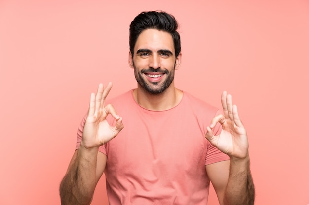 Beau jeune homme sur un mur rose isolé, montrant un signe ok avec les doigts