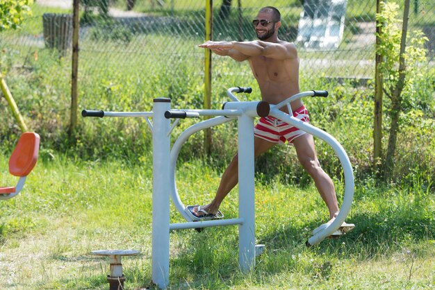 Beau jeune homme musclé s'entraînant sur l'aire de jeux dans le parc