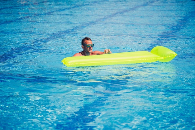 Un beau jeune homme nage sur un matelas gonflable dans une piscine bleue