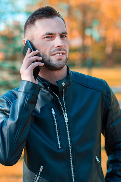 Beau jeune homme parlant au téléphone dans le magnifique parc d'automne. Jeune homme à l'aide de smartphone pour l'appel à l'extérieur à Sunny Day