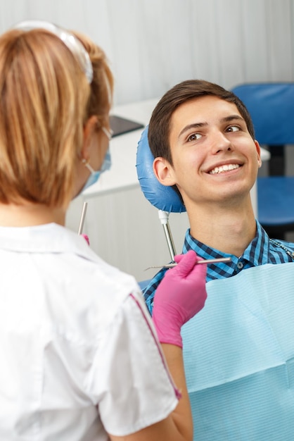 Beau jeune homme passe un examen dentaire au cabinet dentaire. Le dentiste examine un patient avec des outils dentaires