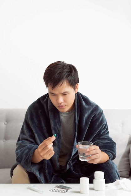 Beau jeune homme avec pilule et verre d'eau à la maison