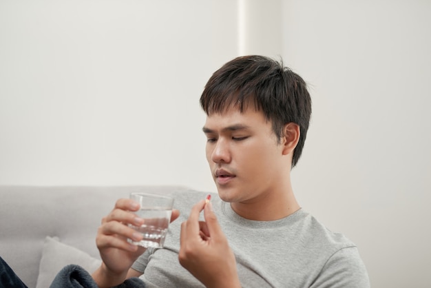 Beau jeune homme avec pilule et verre d'eau à la maison